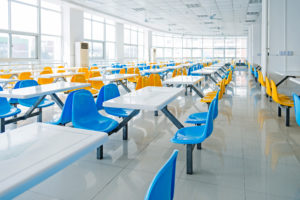 Clean school cafeteria with many empty seats and tables.