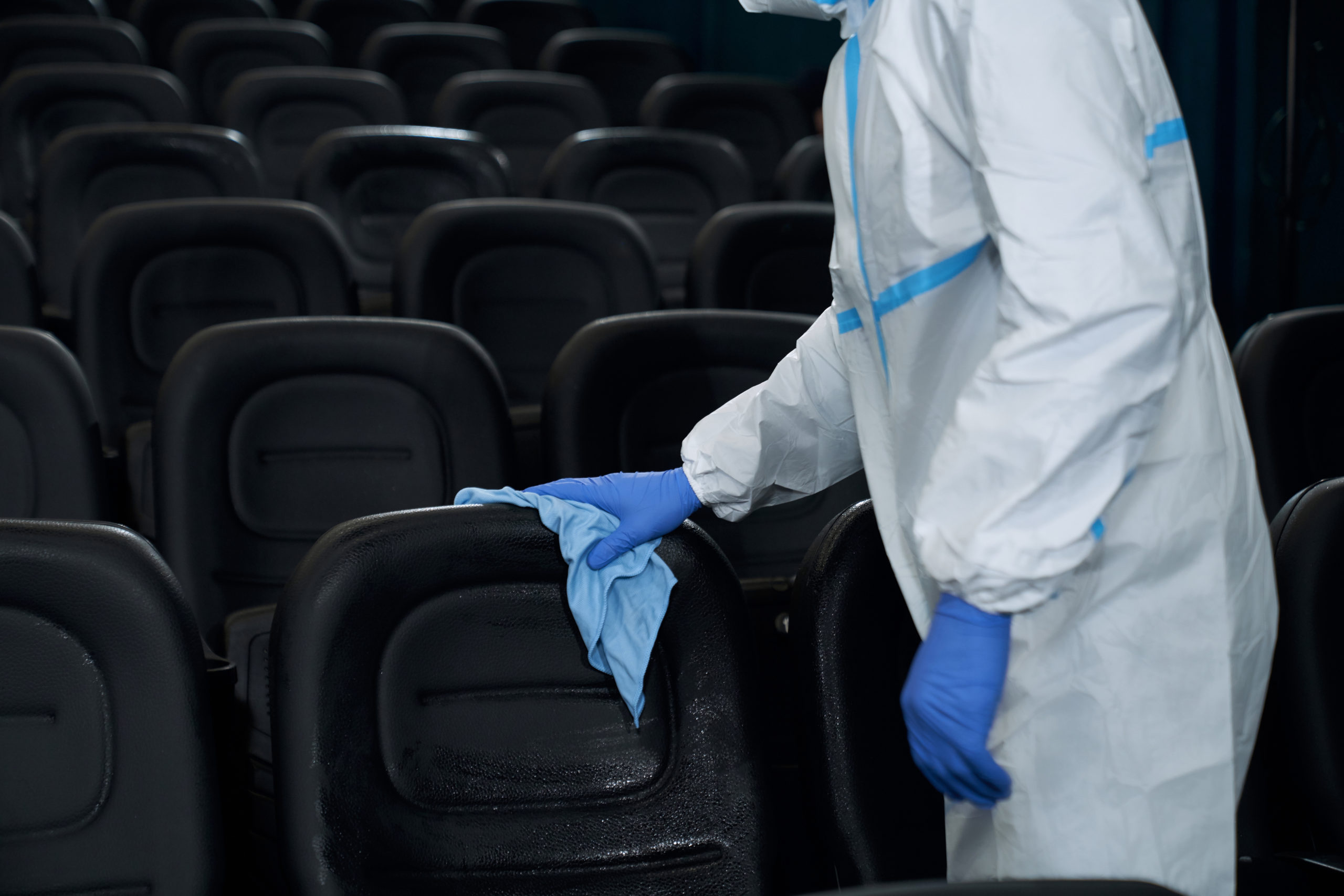 Close up worker in special clothes holding rag and wiping chairs in cinema. Concept of disinfection cinema hall.