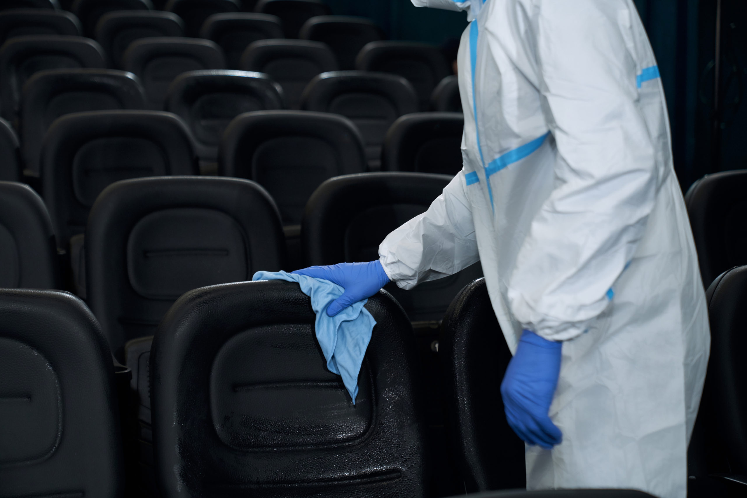 Worker holding rag and wiping chairs in cinema. Close up worker in special clothes holding rag and wiping chairs in cinema. Concept of disinfection cinema hall.